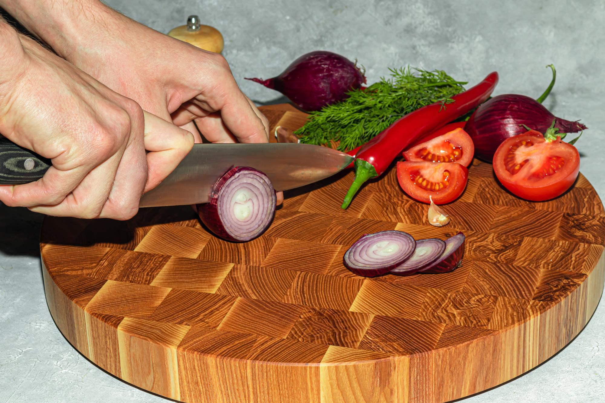 Rankos moksliškai pjausto ingredientus ant medinio pjaustymo lentos